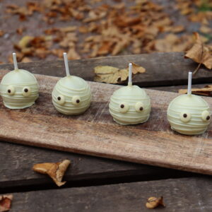 Halloween-Cakepops von Malina Stories in einer 4er-Box: Saftiger Red-Velvet-Kuchen mit cremigem Frischkäse-Frosting, umhüllt von weißer Schokolade und liebevoll von Hand im Halloween-Design dekoriert.